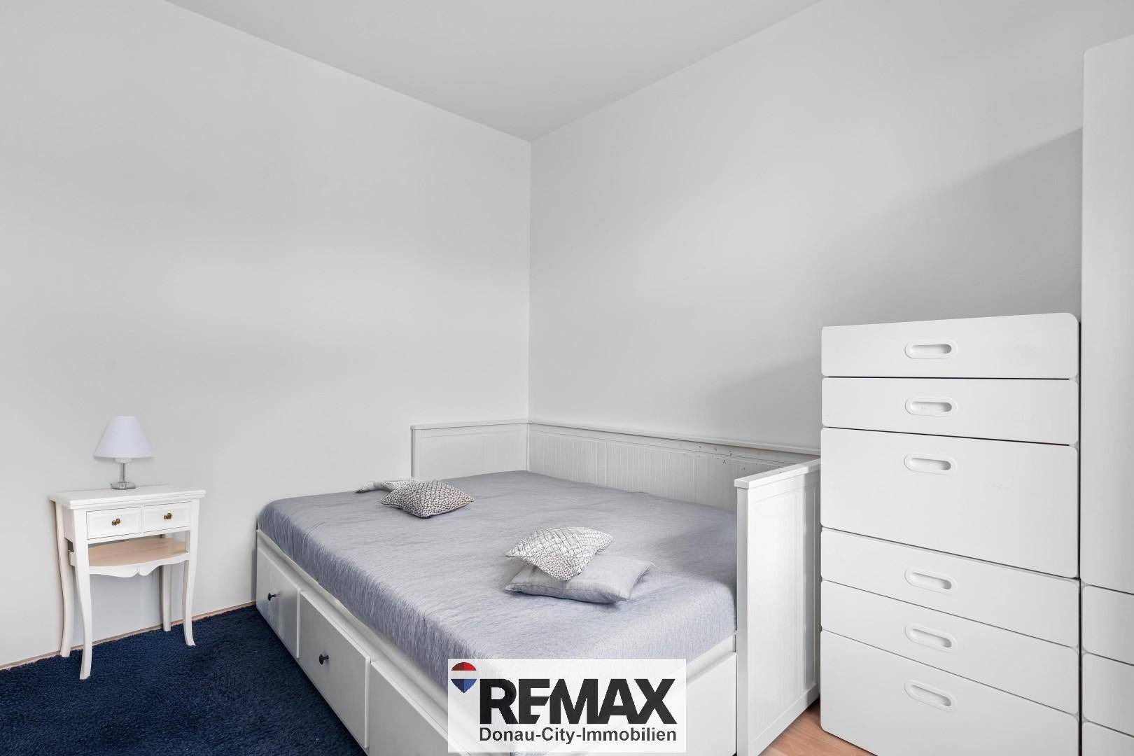 Schlafzimmer mit weißem Bett, blauer Teppichboden und passender Kommode.
