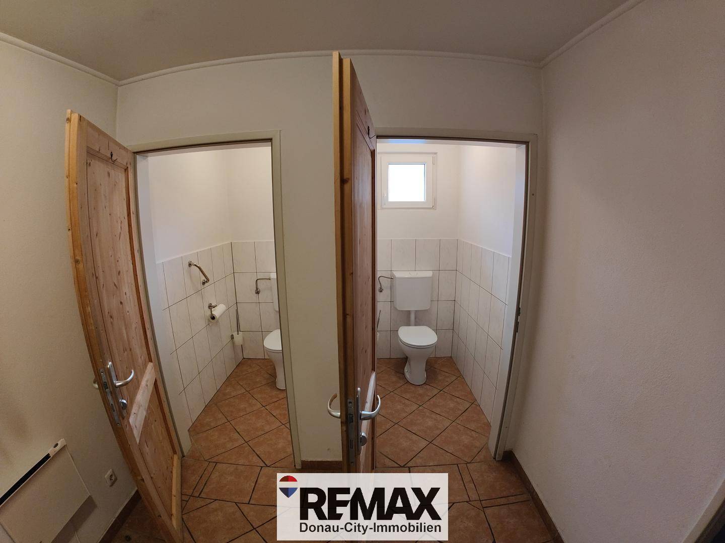 Zwei separate Toilettenräume mit weißen Fliesen und braunem Fliesenboden.