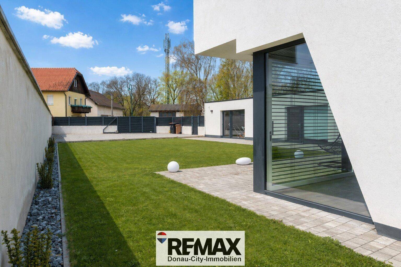 Gepflegter Gartenbereich mit Rasenfläche und gepflasterter Terrasse neben dem modernen Haus.