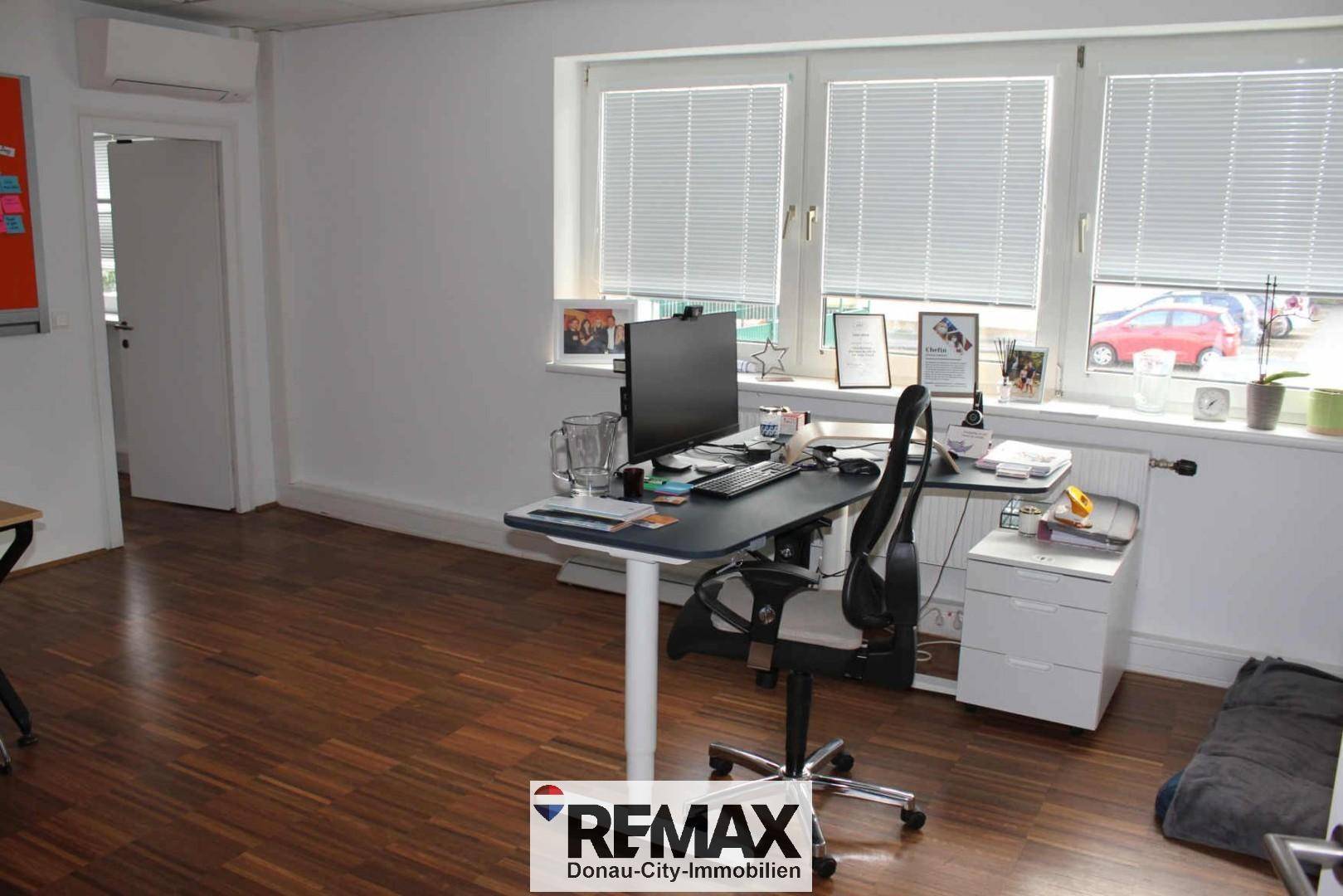 Einzelner Arbeitsplatz in einem hellen Büro mit großen Fenstern und Klimaanlage.