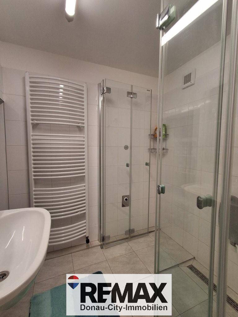 Helles Badezimmer mit Duschkabine, Waschbecken und modernem Handtuchheizkörper.
