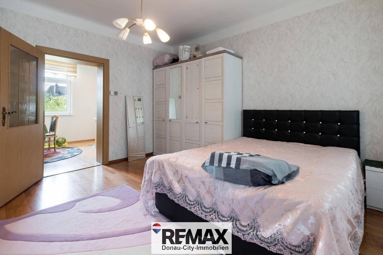 Schlafzimmer mit Doppelbett, großem Kleiderschrank und gemusterter Tapete.