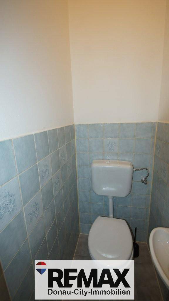 Separate Toilette mit hellblauen Wandfliesen und einem kleinen Waschbecken.