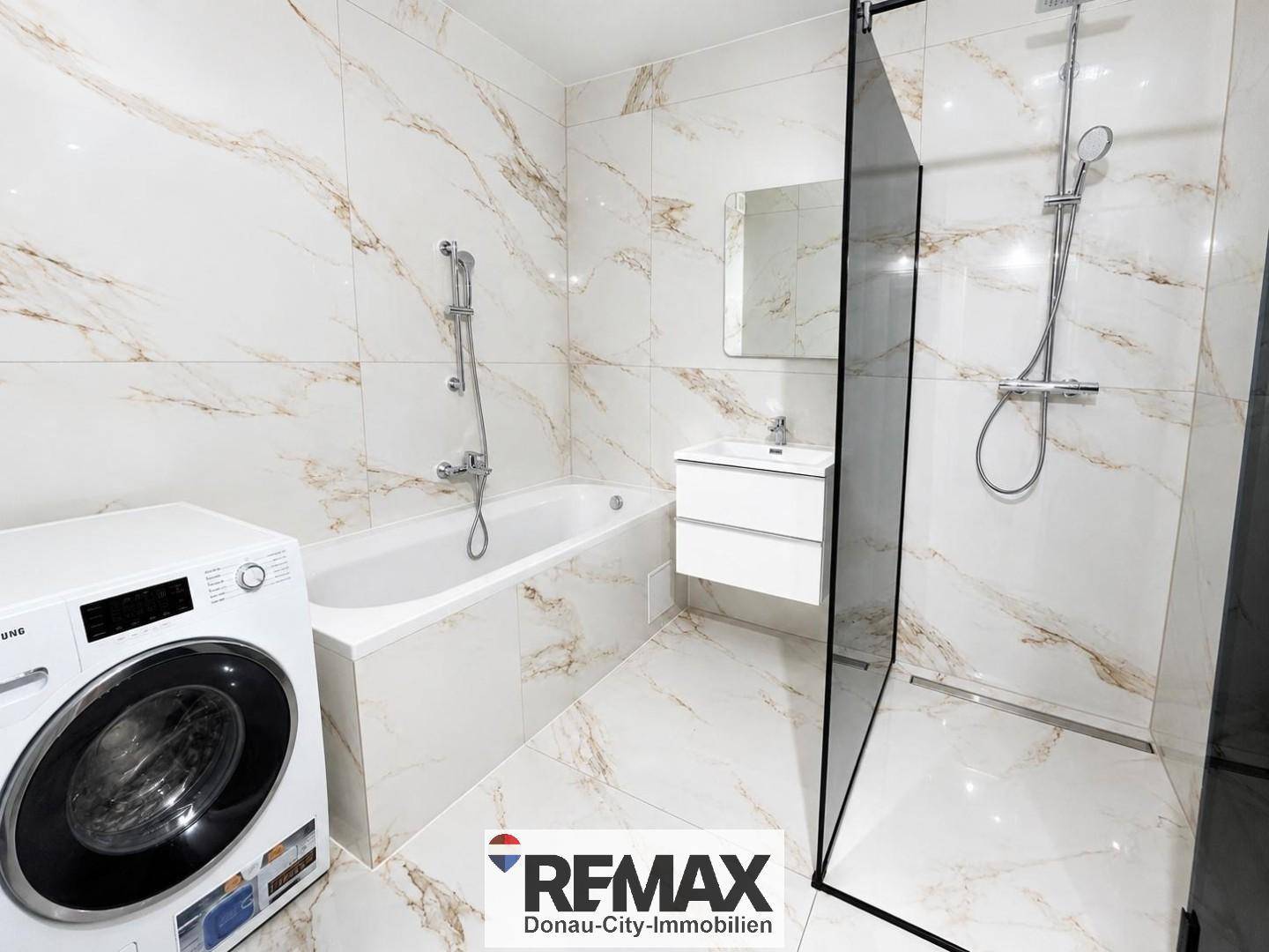 Modernes Badezimmer mit Marmorfliesen, Badewanne, Dusche und integrierter Waschmaschine.