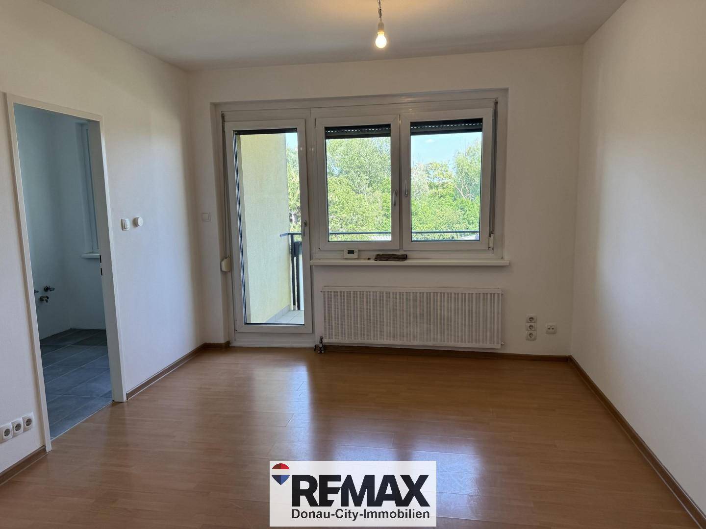 Heller Wohnraum mit Laminatboden, großem Fenster und Zugang zu einem Balkon.