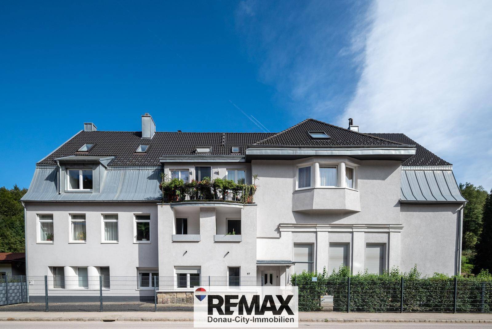 Ansicht der Vorderseite eines Mehrfamilienhauses mit Mansarddach und kleinen Balkonen.