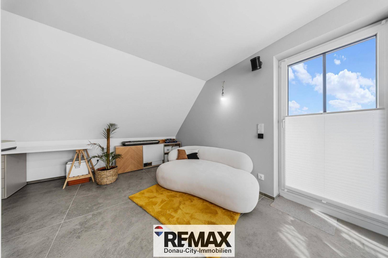 Helles Zimmer im Dachgeschoss mit schräger Wand, modernem Sofa und großem Fenster.