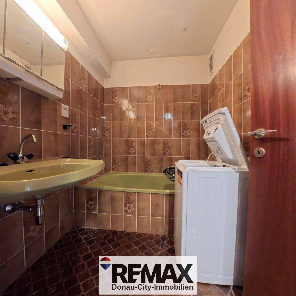 Badezimmer im 80er-Jahre-Stil mit braunen Fliesen, Badewanne und Waschmaschine.