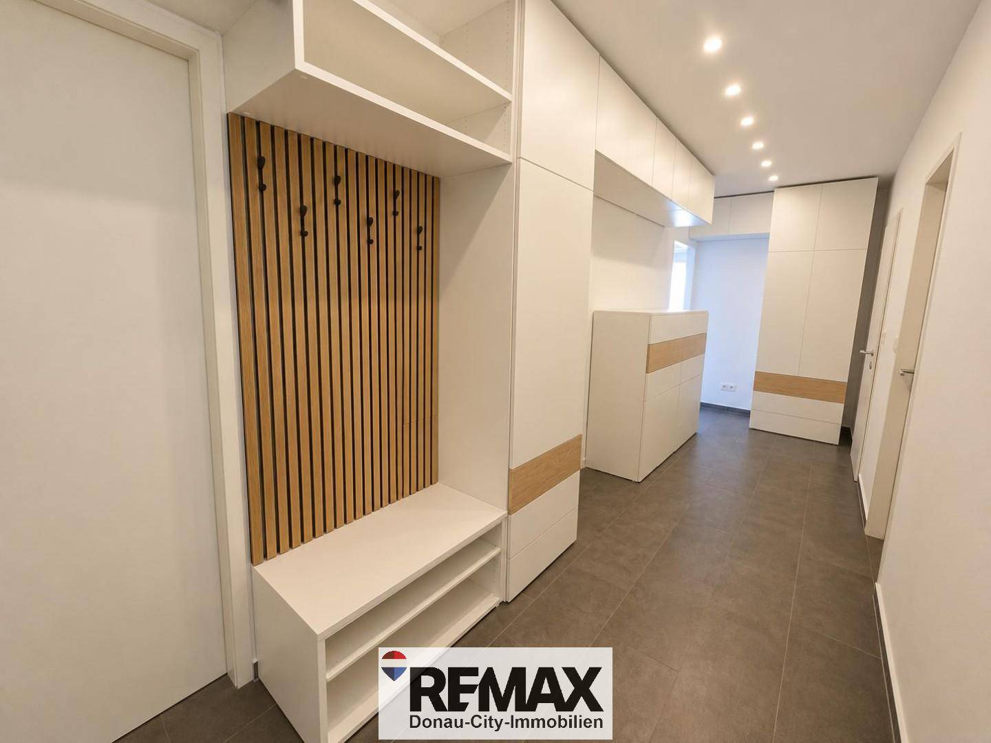 Heller Eingangsbereich mit modernen Einbauschränken, Sitzbank und Garderobe in Holz- und Weißtönen.
