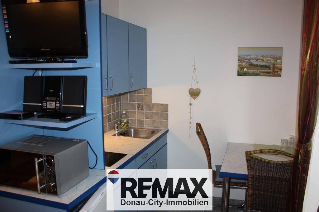Kleine Küchenzeile mit blauen Schränken, Spüle, Kochfeld und Mikrowelle, ideal für ein Apartment.