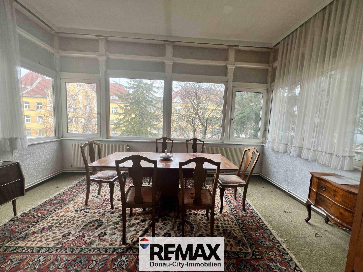 Esszimmer mit großem Holztisch, Stühlen und vielen Fenstern mit Blick ins Grüne.