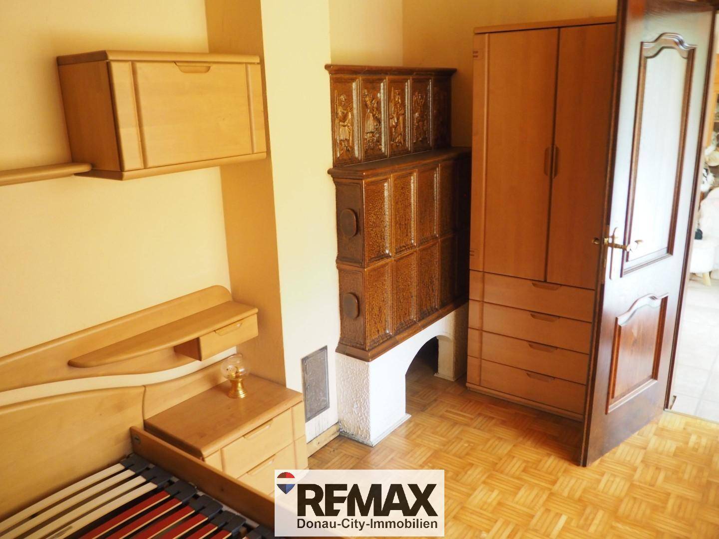 Detailansicht des Schlafzimmers mit Holzschrank und einem traditionellen braunen Kachelofen.