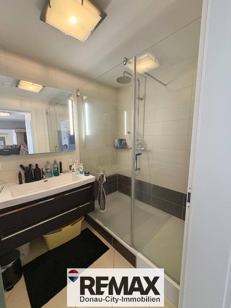 Modernes Badezimmer mit Duschkabine, Einzelwaschbecken und hellen Wand- und Bodenfliesen.
