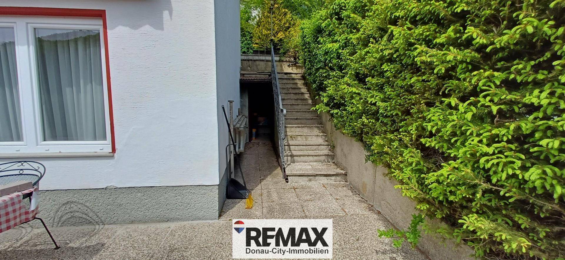 Außentreppe führt entlang einer grünen Hecke zum oberen Bereich des Grundstücks.