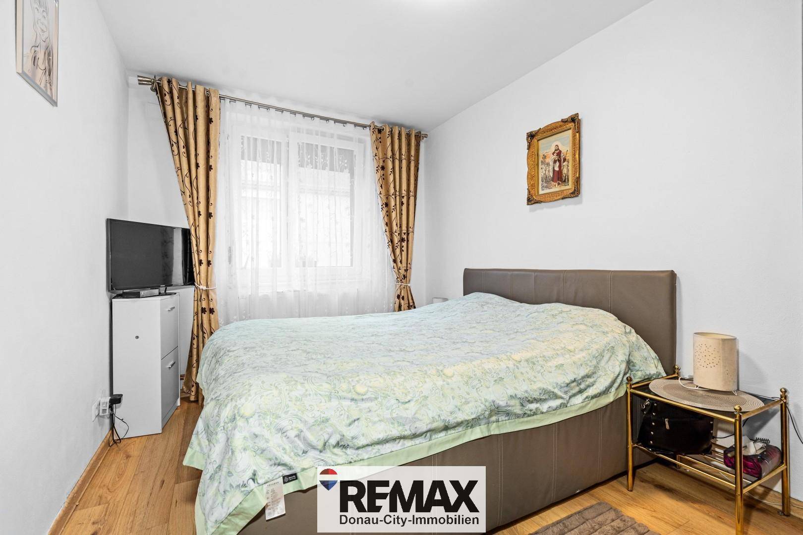 Gemütliches Schlafzimmer mit Doppelbett, Holzboden und Vorhängen vor dem Fenster.