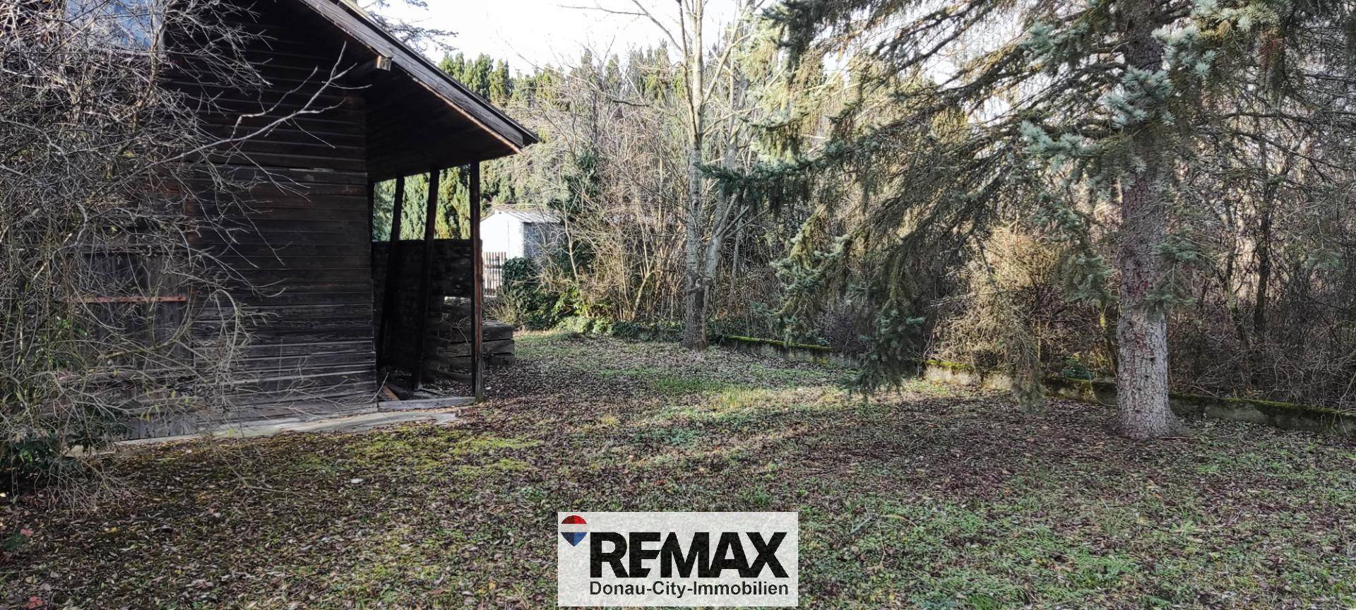 Rustikales Holzhaus im Gartenbereich umgeben von Bäumen und Natur.
