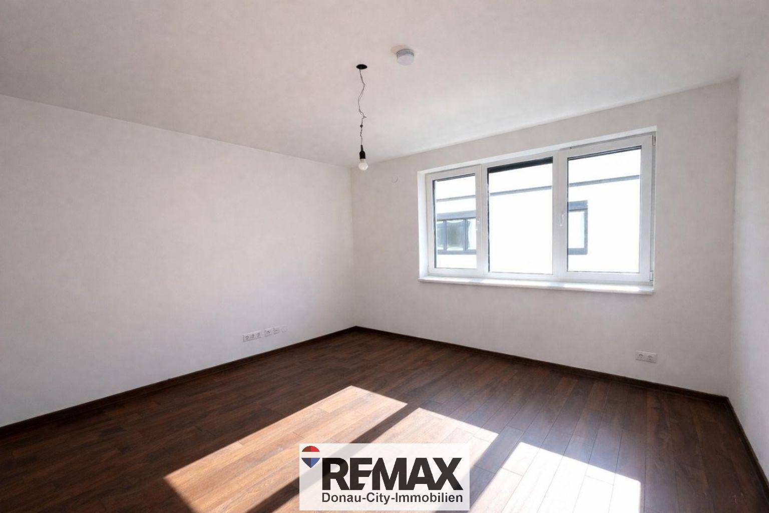 Geräumiges Zimmer mit dunklem Holzboden und großem Fenster, ideal für vielfältige Nutzungsmöglichkeiten.
