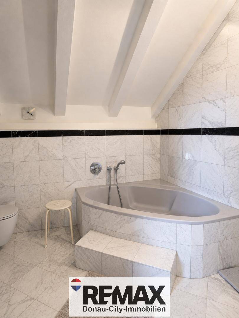 Helles Badezimmer mit Marmorfliesen, einer Eckbadewanne und Dachschrägen, funktional eingerichtet.