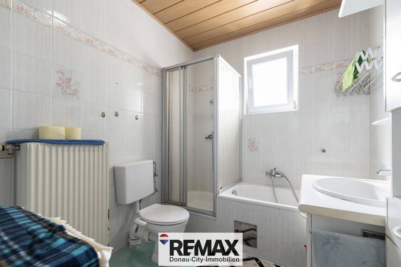Badezimmer mit Badewanne, Duschkabine, WC und Fenster, gefliest in hellen Farben.