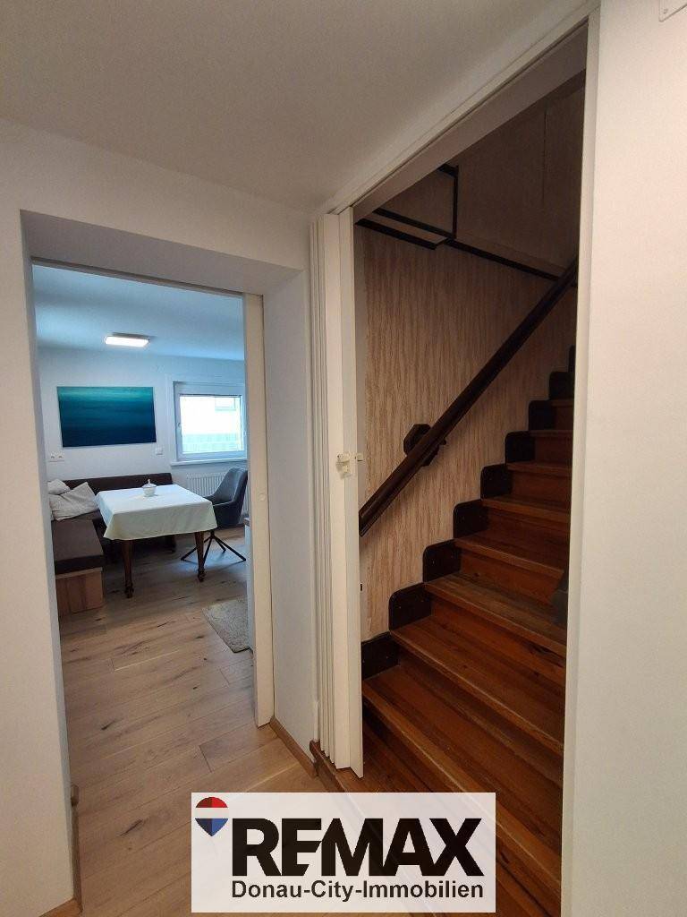 Flur mit Holztreppe, die in das Obergeschoss führt, und Zugang zu einem Essbereich.