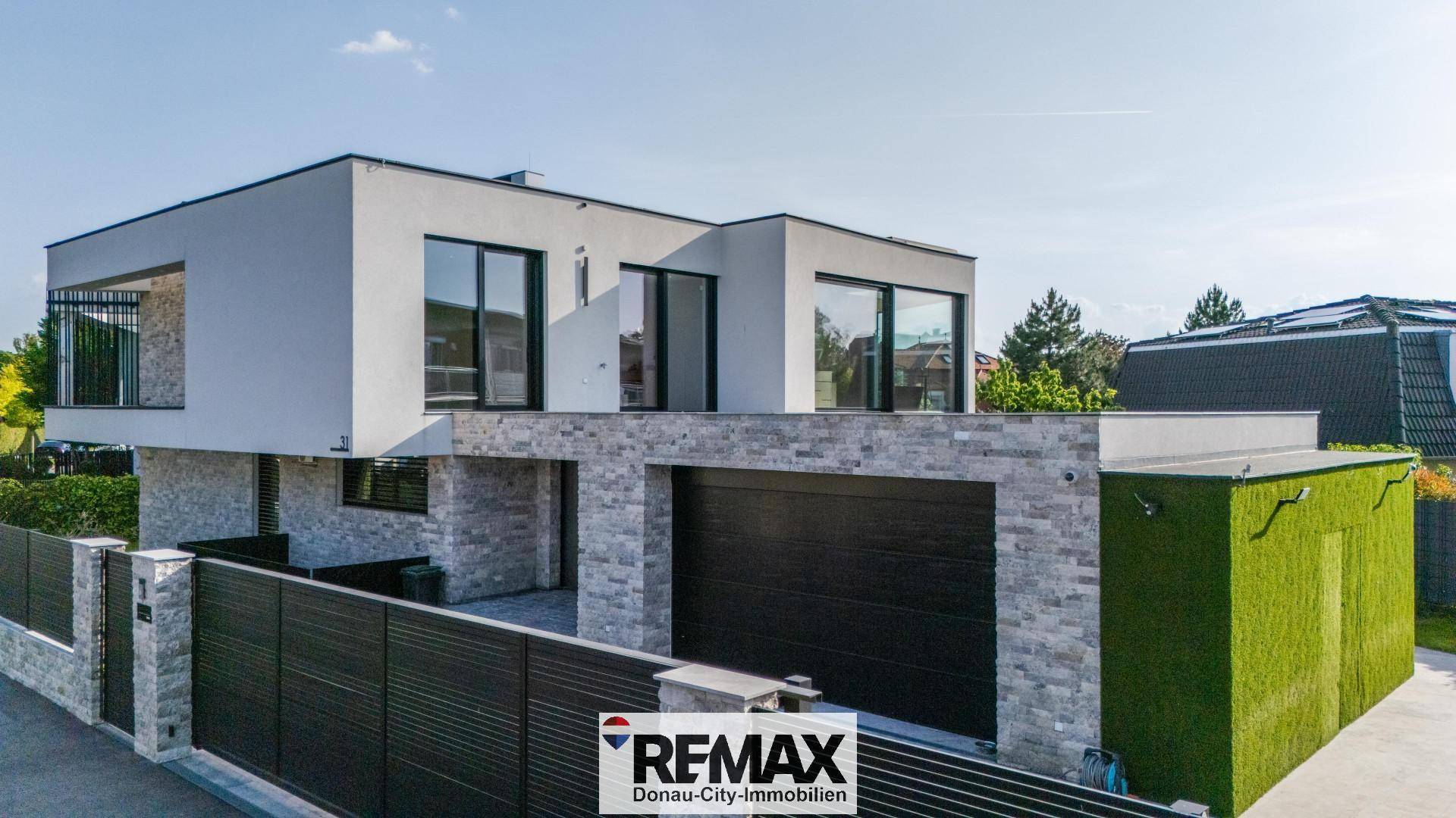 Moderne Architektur mit klaren Linien, großen Fenstern und einer Garage. Die Fassade kombiniert Putz und Steinverkleidung.