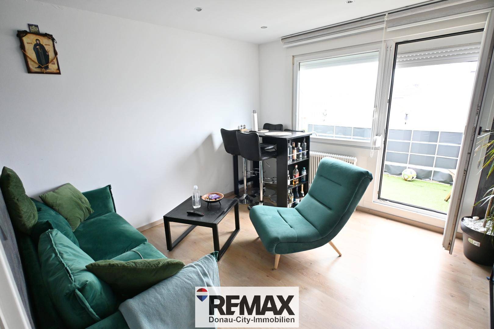 Gemütliches Wohnzimmer mit grüner Couch, Sessel und Zugang zum Balkon, hell und modern eingerichtet.