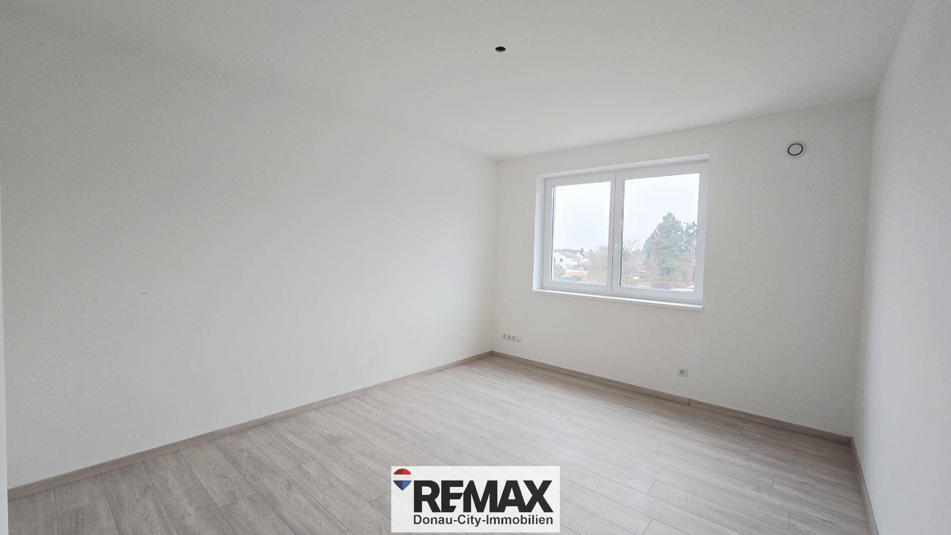 Helles, leeres Zimmer mit Laminatboden und einem großen Fenster, ideal als Schlafzimmer.