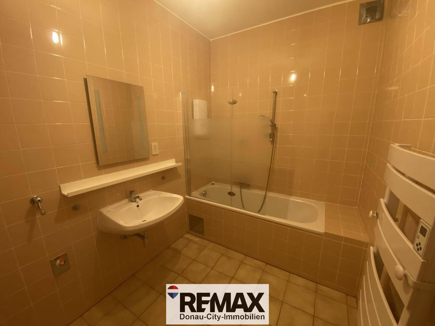 Gefliestes Badezimmer mit Badewanne, Waschbecken und beheiztem Handtuchhalter in warmen Farbtönen.