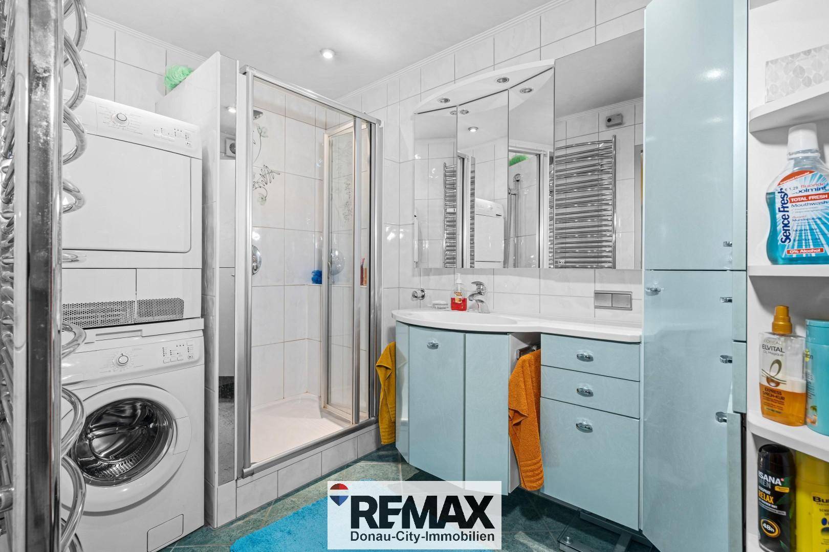 Badezimmer mit Dusche, Waschmaschine und Trockner sowie blauen Schränken.