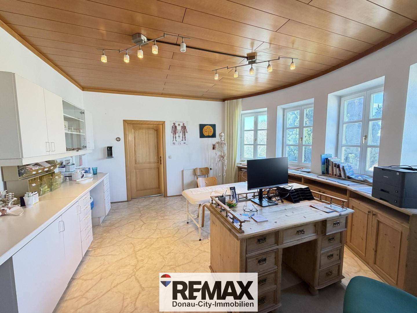 Büro oder Behandlungszimmer mit Holzdecke, Schreibtisch und Einbauschränken.