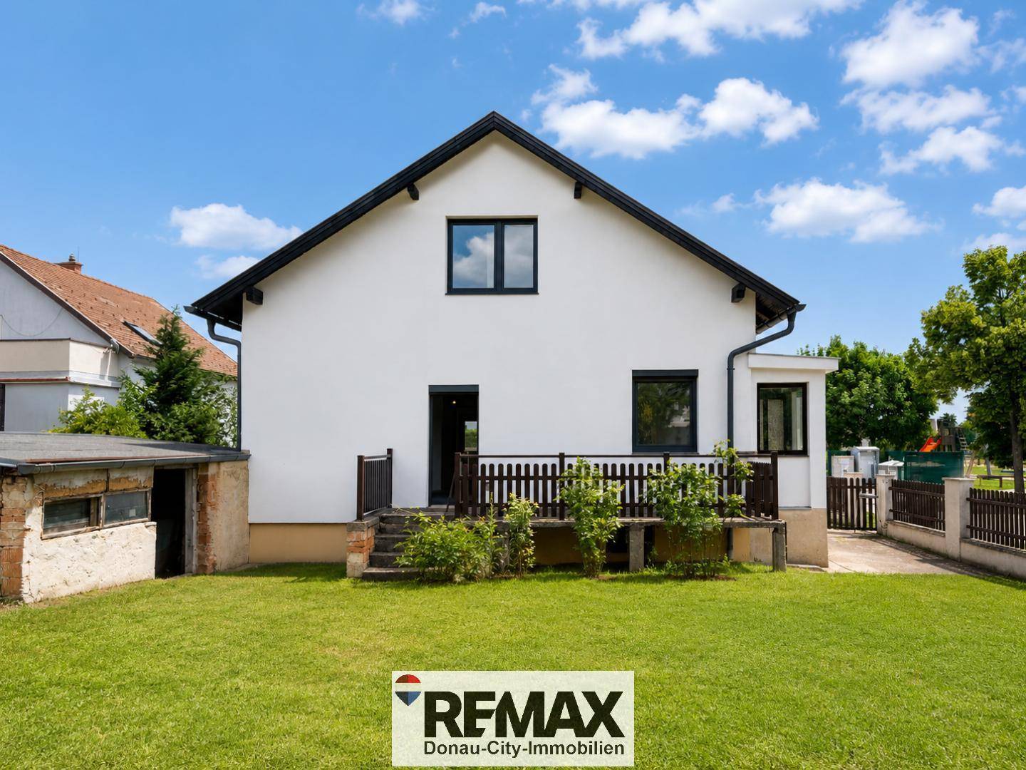 Rückansicht des Hauses mit gepflegtem Rasen, kleiner Holzterrasse und Gartenbereich.