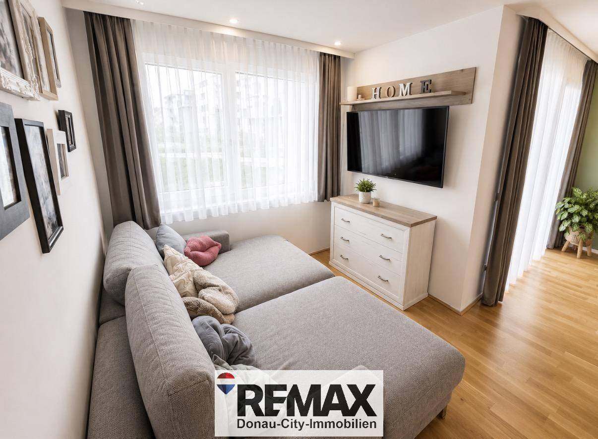 Gemütliches Wohnzimmer mit großem Sofa, Fernseher und hellen Fenstern.