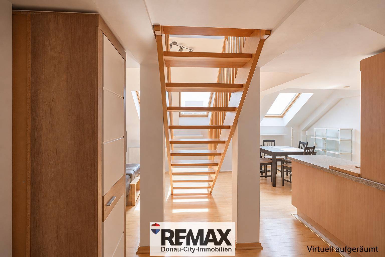 Offener Wohnbereich mit heller Holztreppe, die die Ebenen verbindet, und Essbereich im Hintergrund.