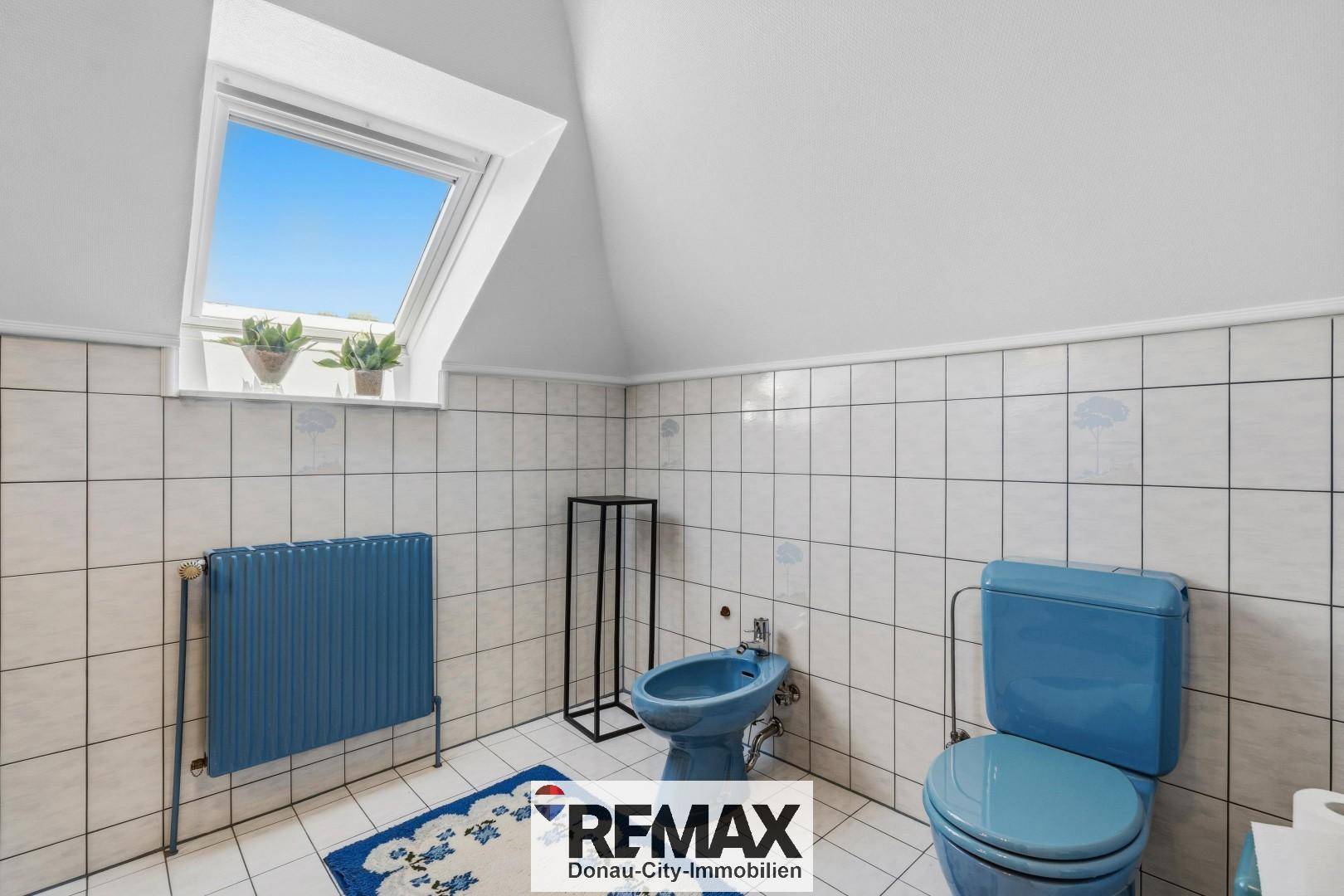 Badezimmer im Dachgeschoss mit blauen Sanitärobjekten, Fliesen und Dachfenster.