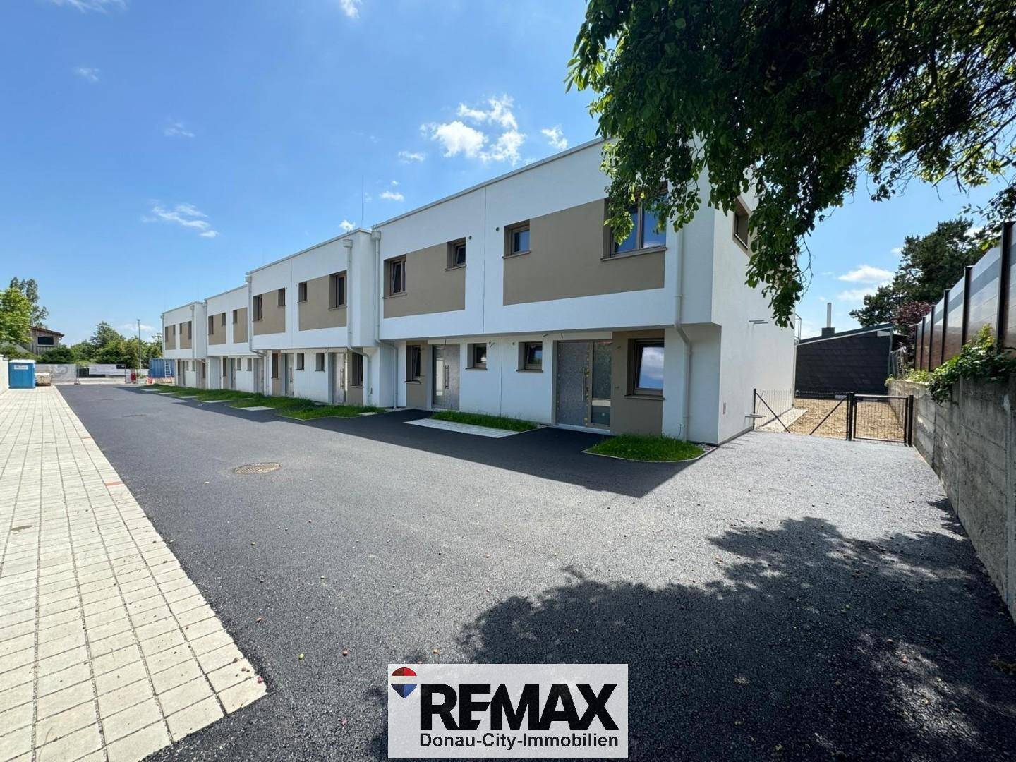 Reihe moderner Neubauten mit schlichter Fassade und neu angelegter Zufahrt unter sonnigem Himmel.