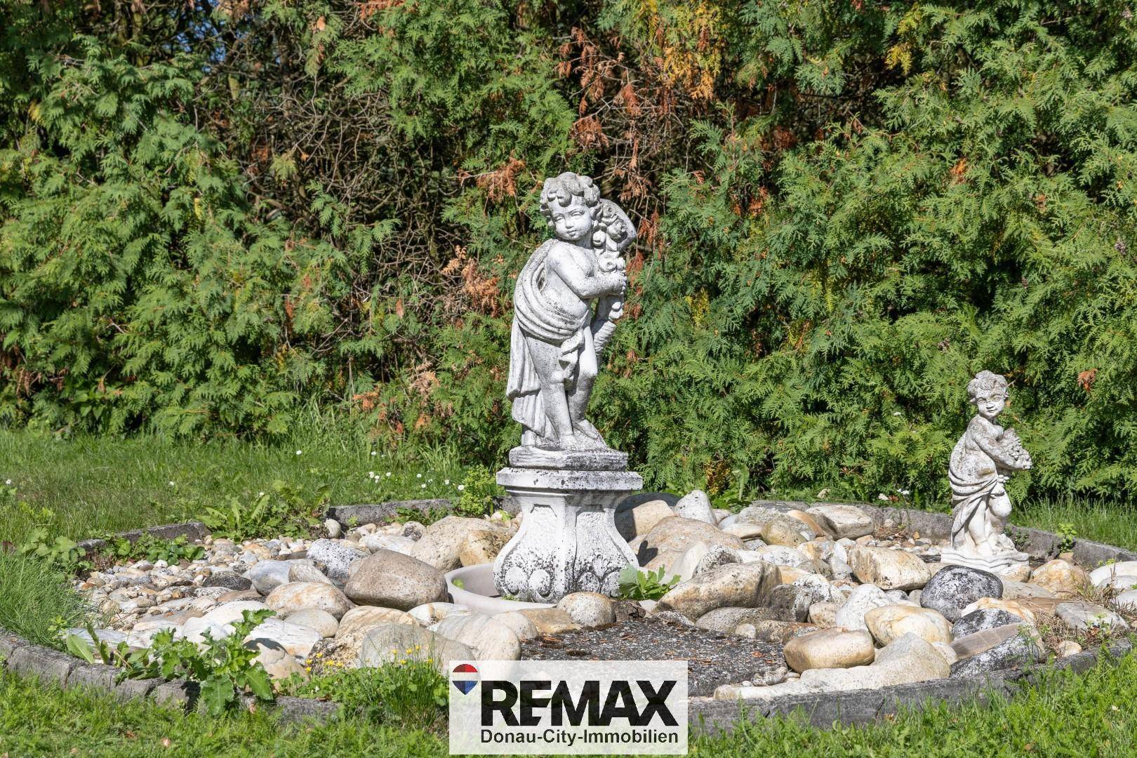Gartenbereich mit einer klassischen Steinstatue, umgeben von einem dekorativen Steingarten.