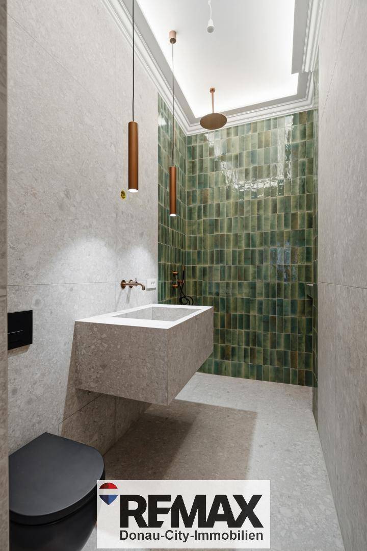 Stilvolles Badezimmer mit grüner Duschwand, modernem Waschbecken und schwarzer Wandtoilette.