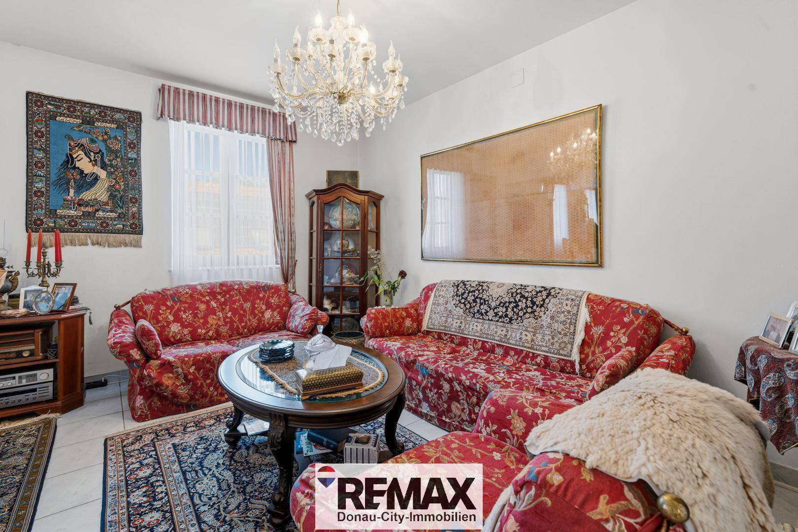 Gemütliches Wohnzimmer mit roten Sofas, orientalischen Teppichen und einem Kronleuchter.