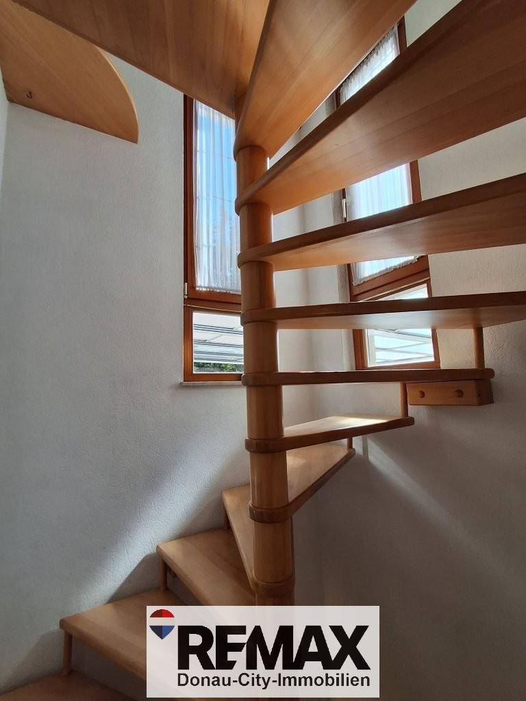 Elegante Holzwendeltreppe mit Fenstern, die den Aufgang hell und einladend gestalten.