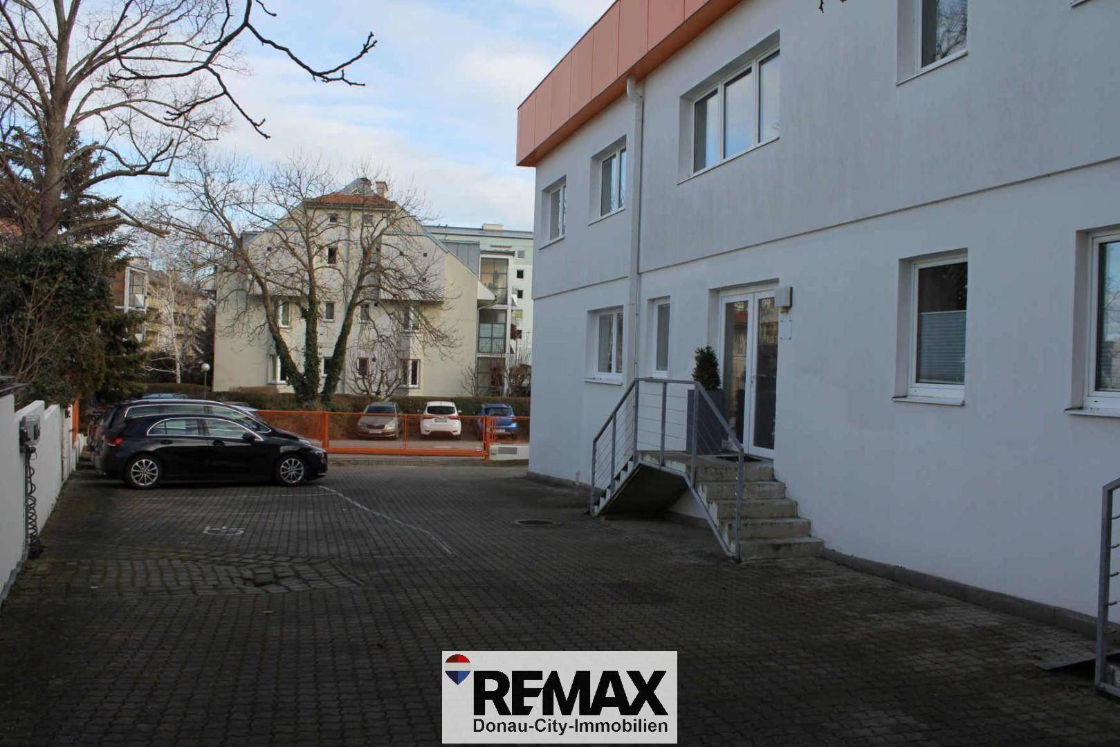Außenbereich des Gebäudes mit Parkplätzen, Zufahrt und umliegender Bebauung.