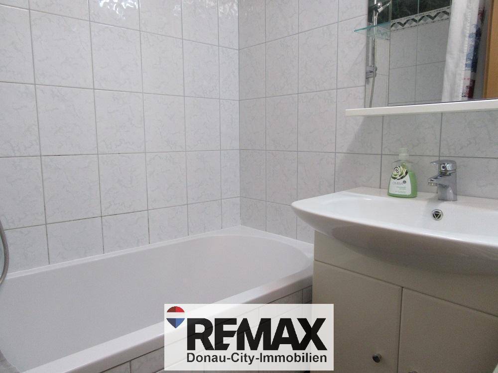 Gefliestes Badezimmer mit Badewanne, Waschbecken und Spiegel.