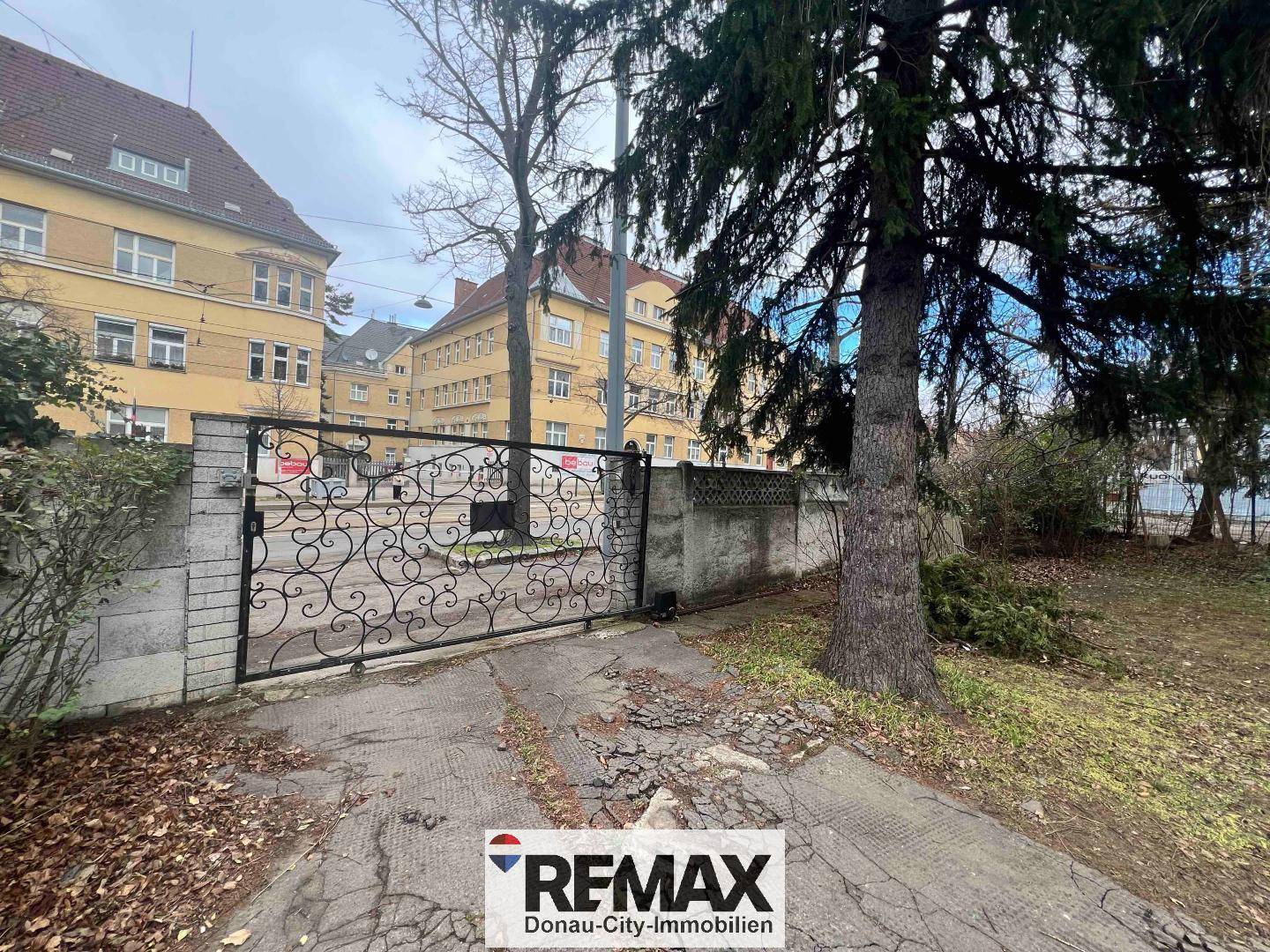 Einfahrt mit schmiedeeisernem Tor und Blick auf die umliegenden Gebäude in der Nachbarschaft.