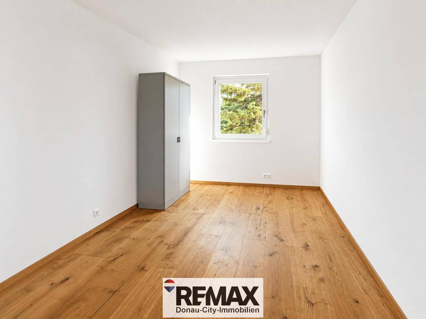 Helles Schlafzimmer mit Holzboden und einem Fenster mit angenehmem Blick ins Grüne.