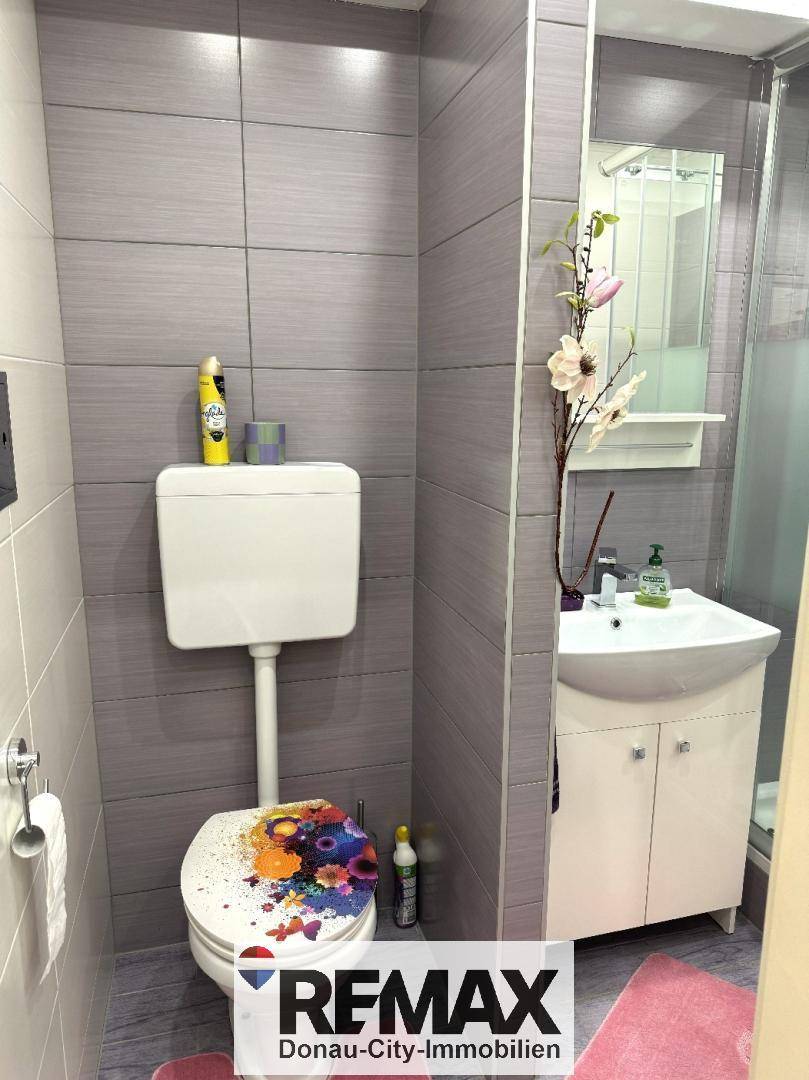 Badezimmer mit Toilette, Waschbecken und Duschkabine, ausgestattet mit modernen grauen Fliesen.