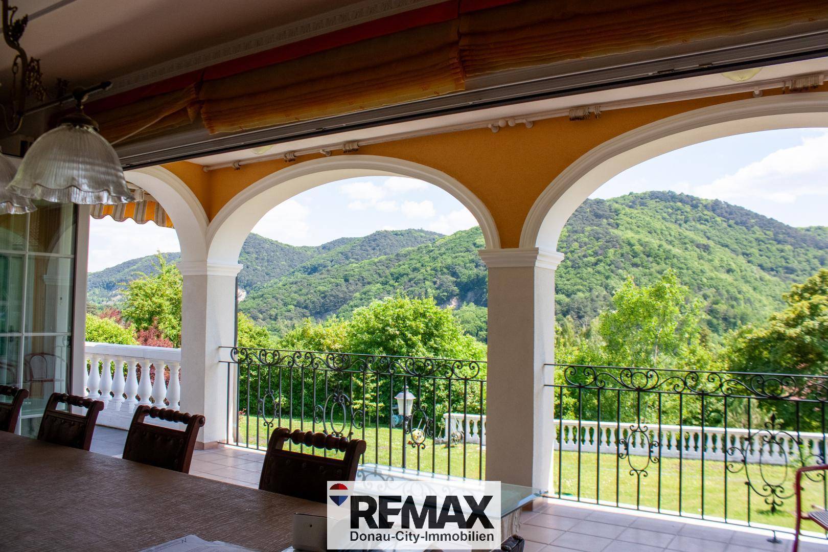 Überdachte Loggia mit Bögen und schmiedeeisernem Geländer bietet einen weiten Blick auf die grünen Berge.
