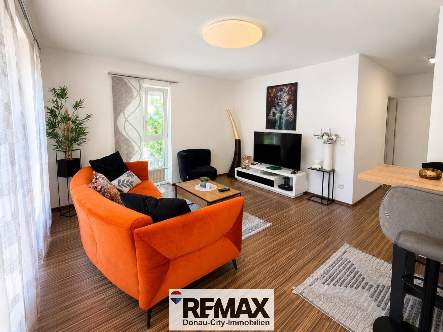 Gemütliches Wohnzimmer mit orangefarbenem Sofa, Holzboden und Blick ins Grüne.