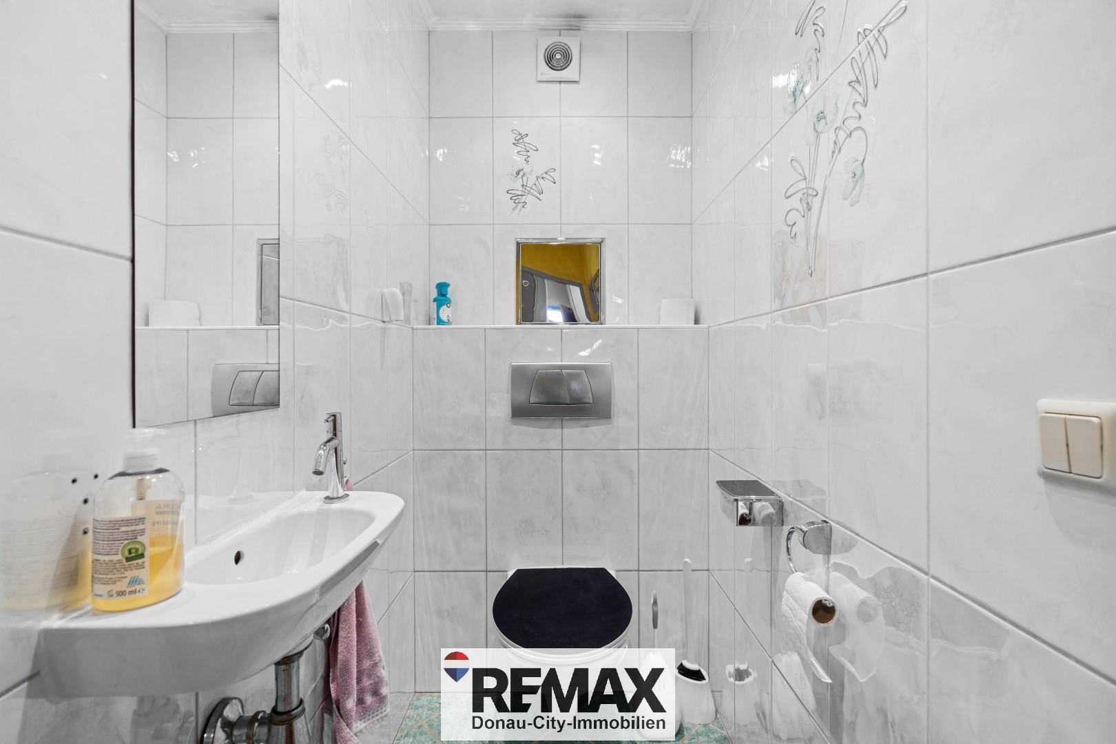 Separates WC mit Wand-WC, kleinem Waschbecken und weißen Fliesen.