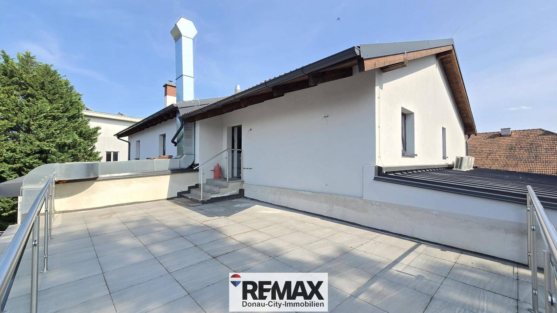Großzügige Dachterrasse mit modernen Fliesen und Edelstahlgeländer, angrenzend an das Gebäude.