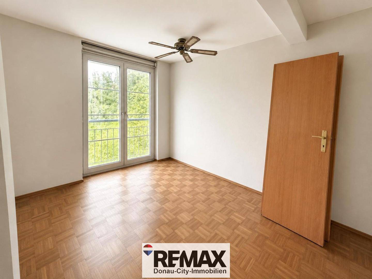 Helles Schlafzimmer mit Parkettboden, Deckenventilator und Zugang zu einem französischen Balkon.