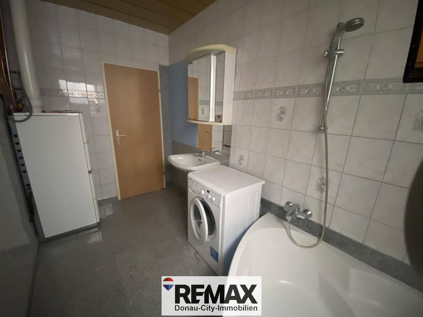 Badezimmer mit Badewanne, Waschbecken, Waschmaschine und Fliesen an Wänden und Boden.